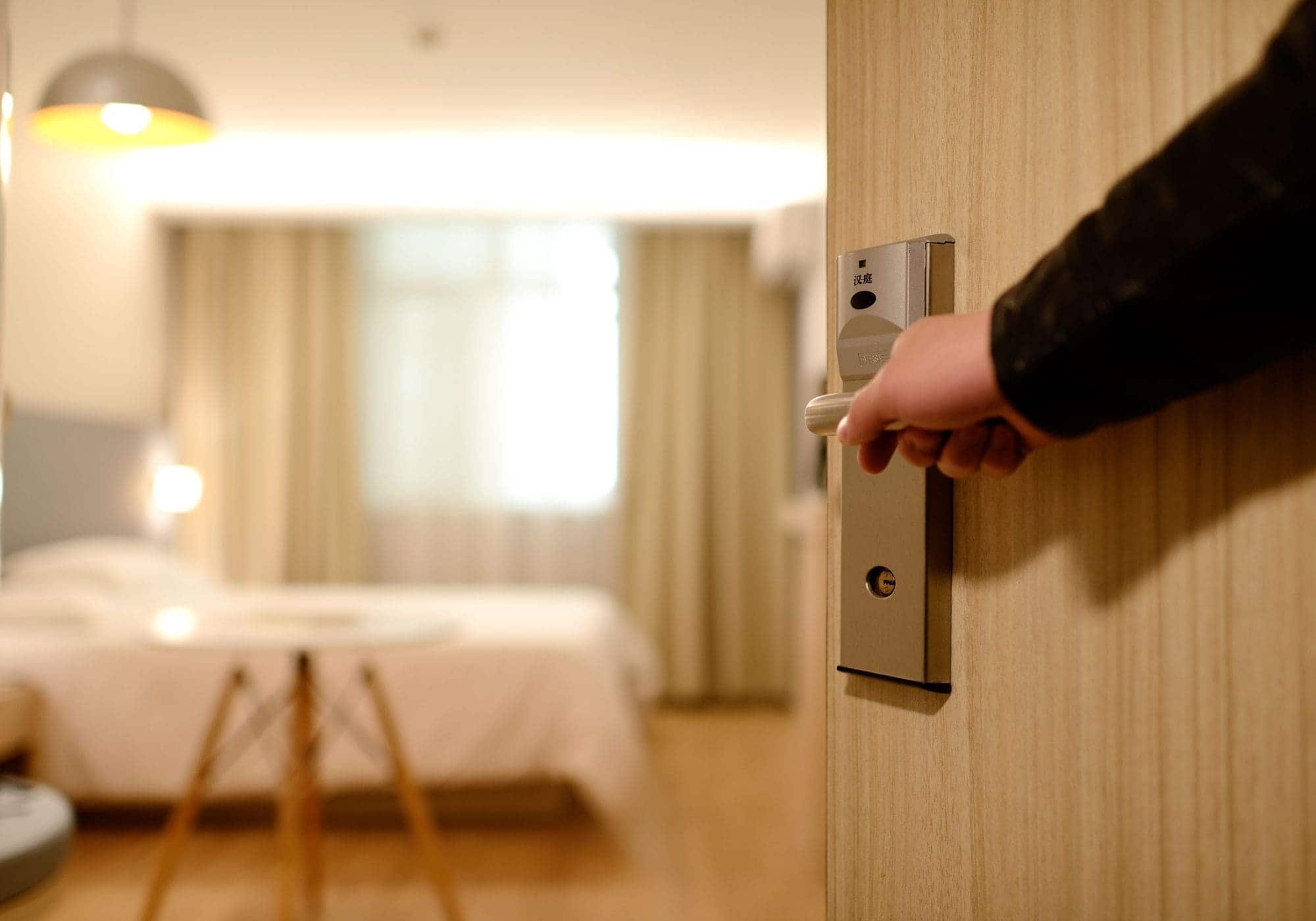 A hand opening a hotel room door, the quiet moment of arrival.