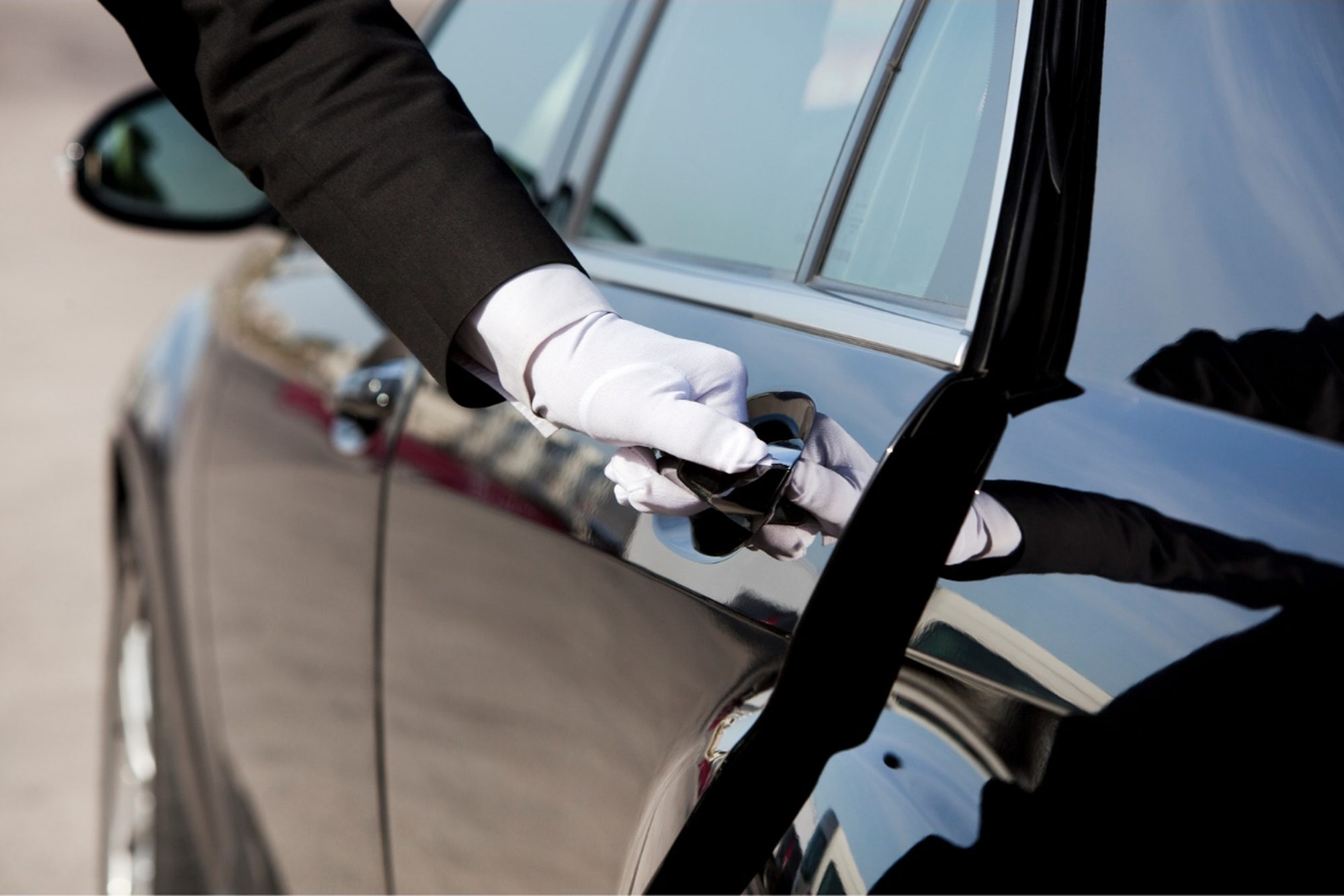 A white-gloved chauffeur opening a luxury car door for an arriving guest.