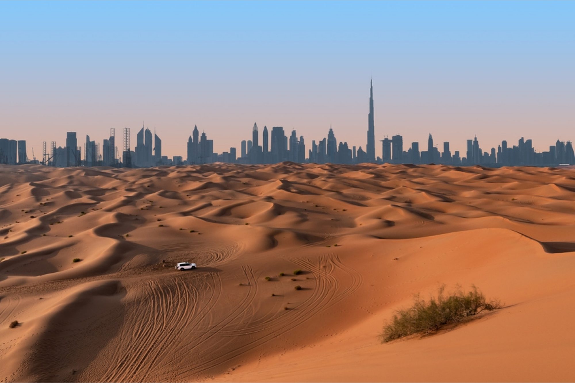 Dubai’s skyline rising beyond golden desert dunes at sunset.