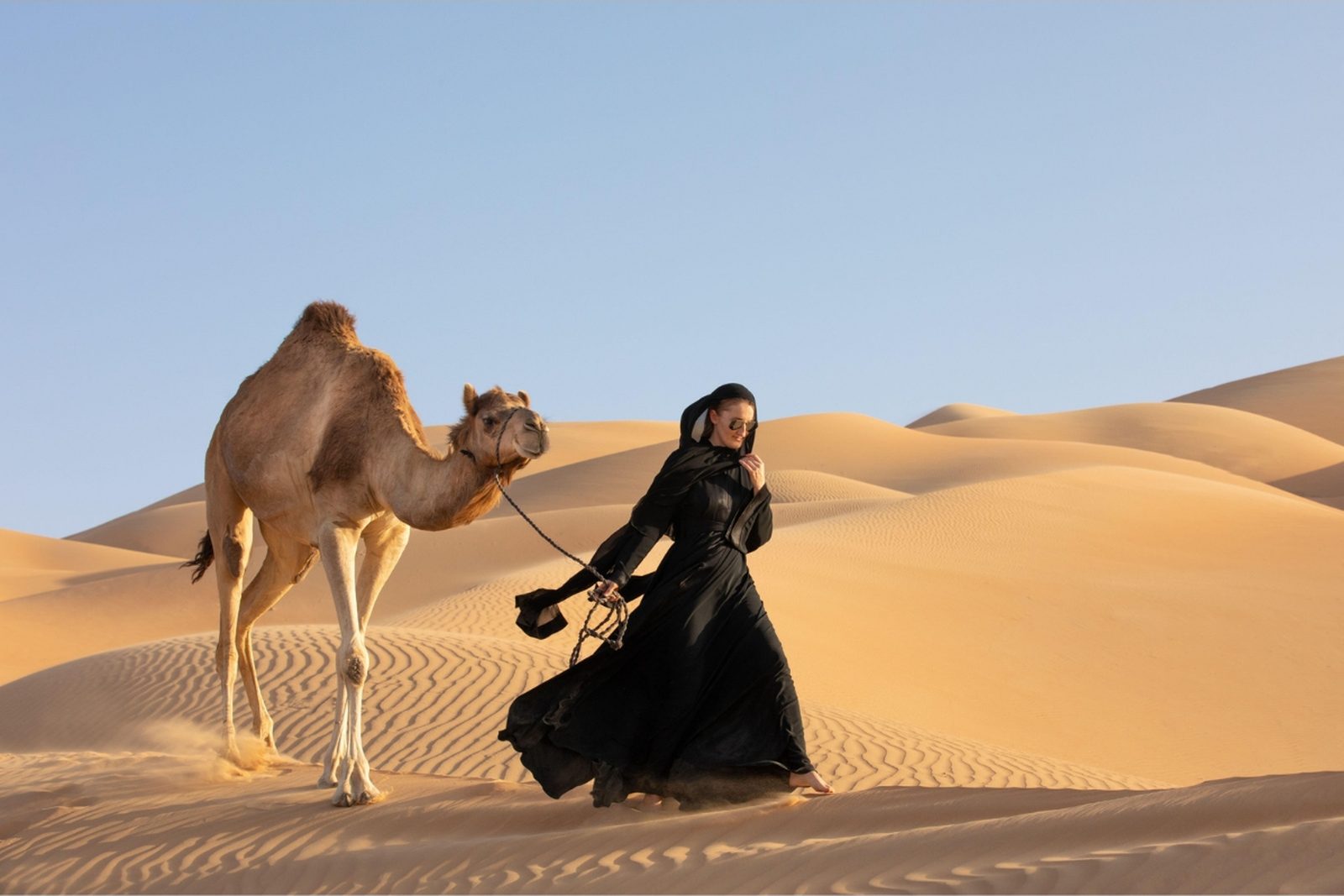 A camel and a guide in traditional dress on the Dubai dunes at sunset.