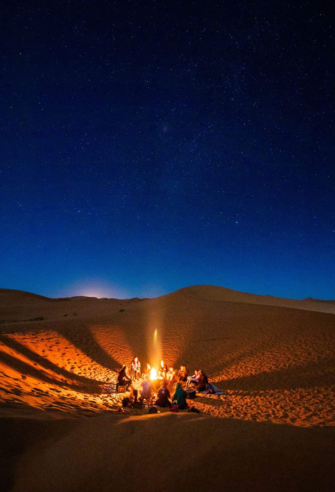 Quiet desert at dusk with a low warm light on the horizon and a star-touched sky above.