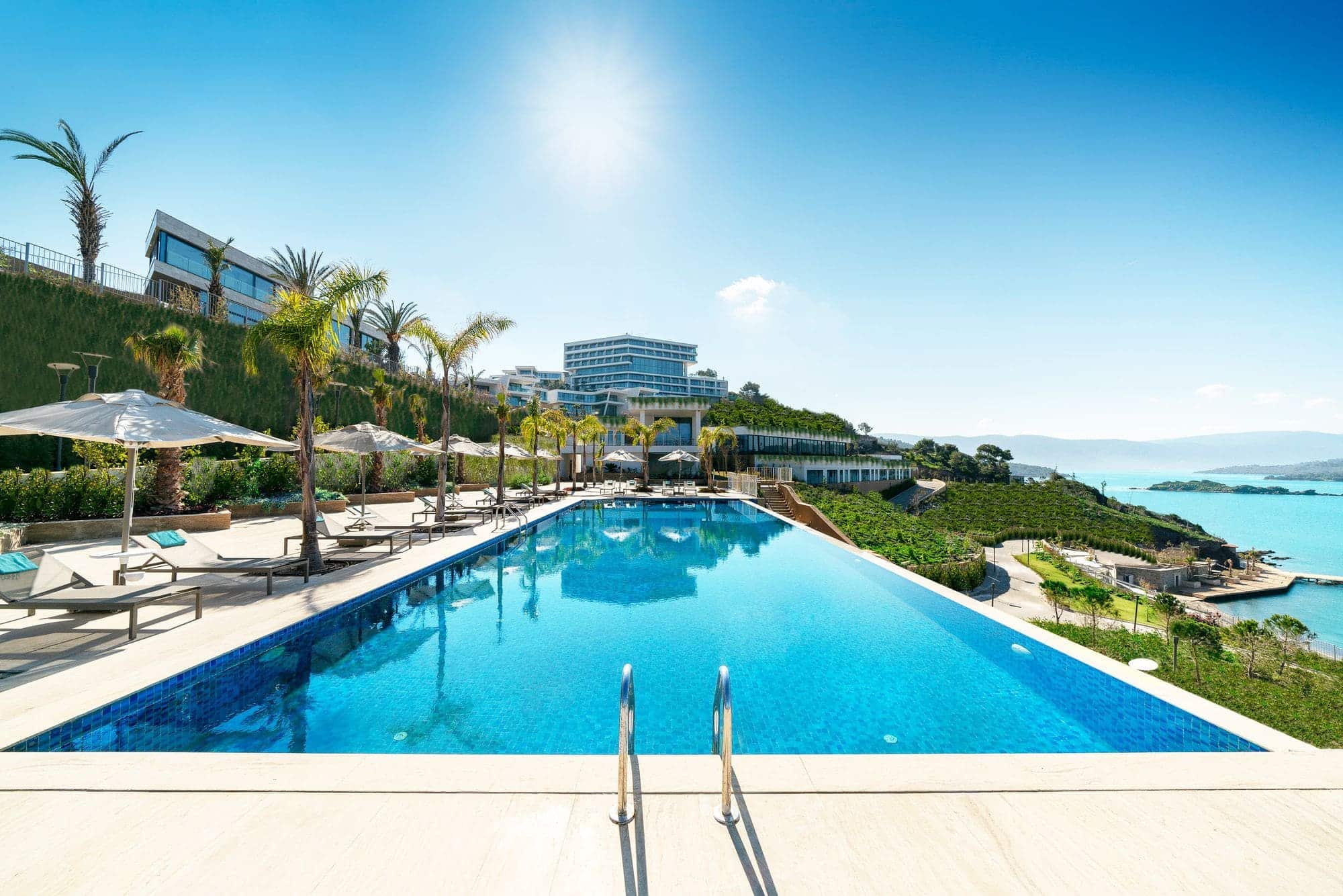 A resort swimming pool on a terrace overlooking the sea in warm daylight.