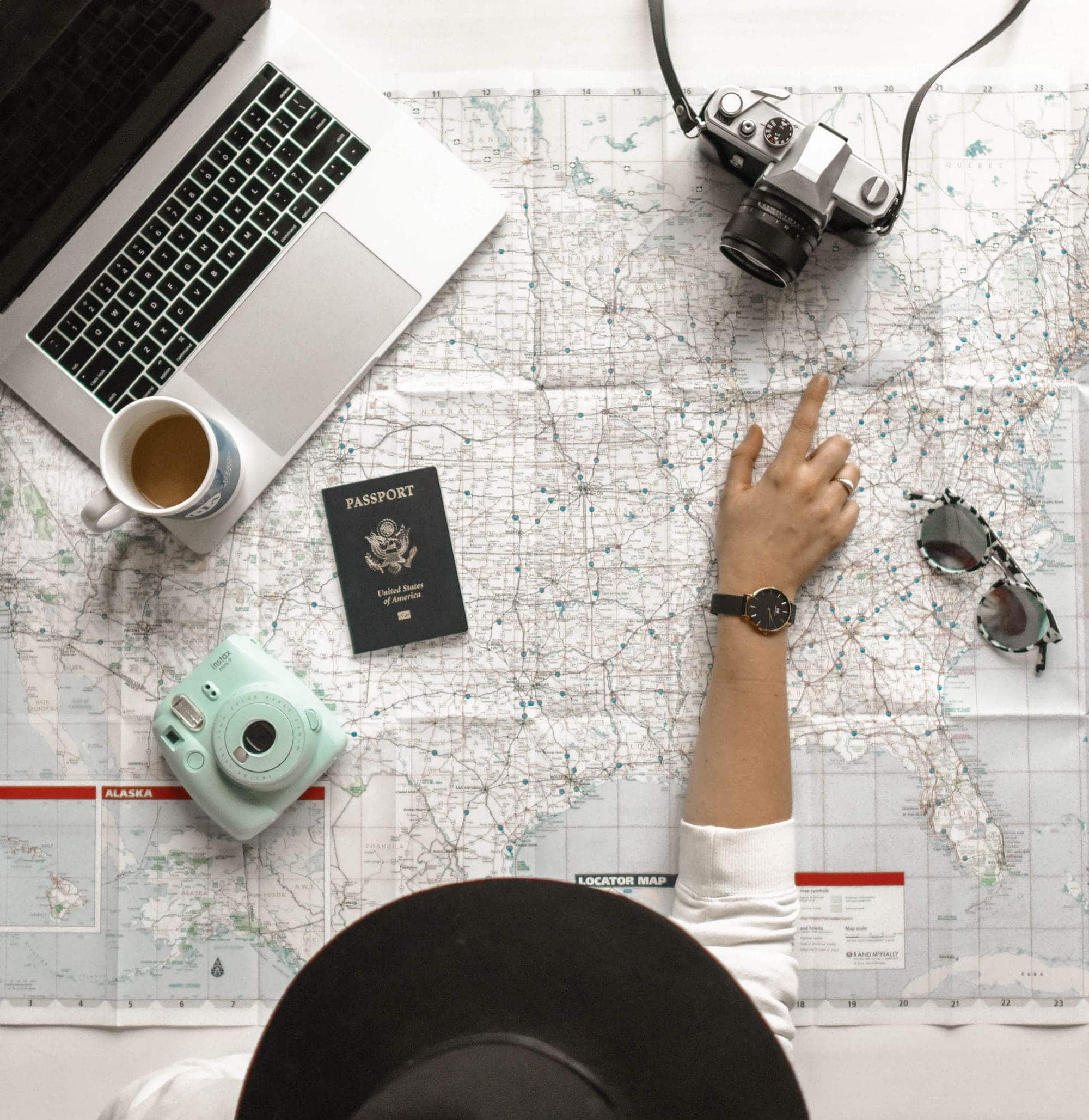 Travel essentials laid out for planning, passport, watch, map and coffee.